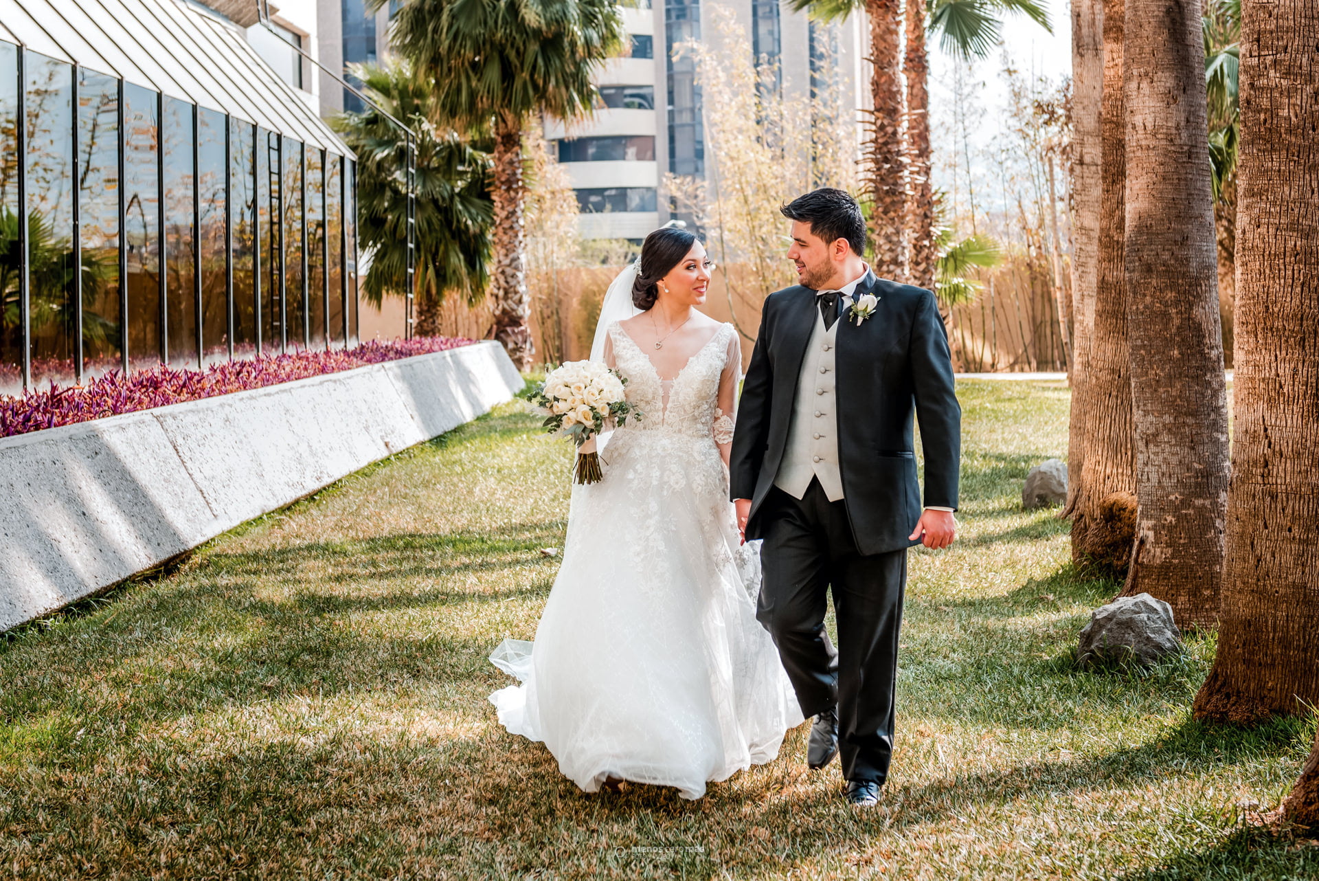 Diana y Antonio, radiantes de felicidad, caminan tomados de la mano en los jardines del Hotel MS Milenium antes de su boda. La luz del sol los baña creando una atmósfera mágica. Fotografía por "menosceromás fotografía".