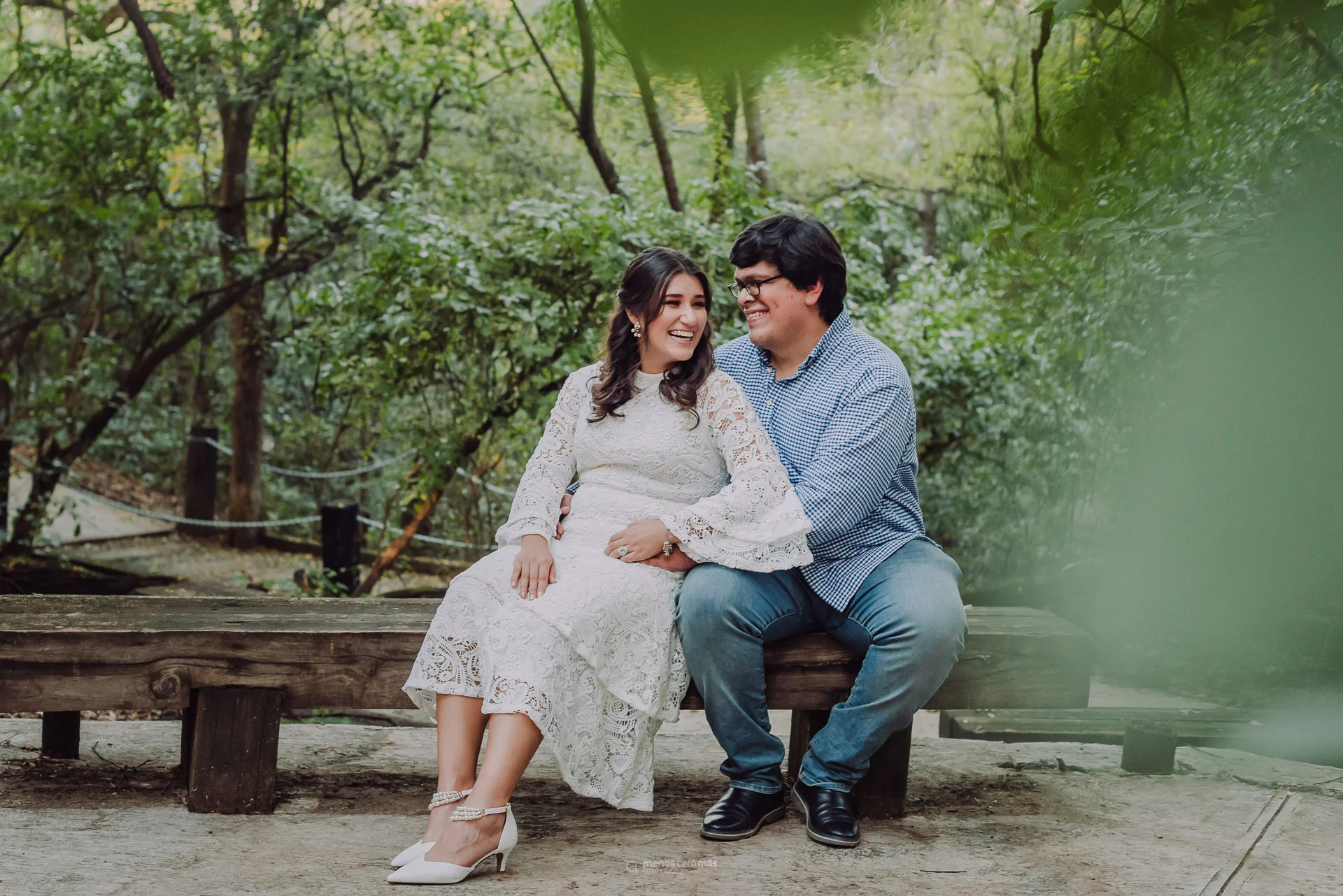 Imagen de Sarahi y Carlos en una sesión casual de fotos en el Gran Parque Río La Silla, sentados en una banca del parque con el andador y árboles al fondo.