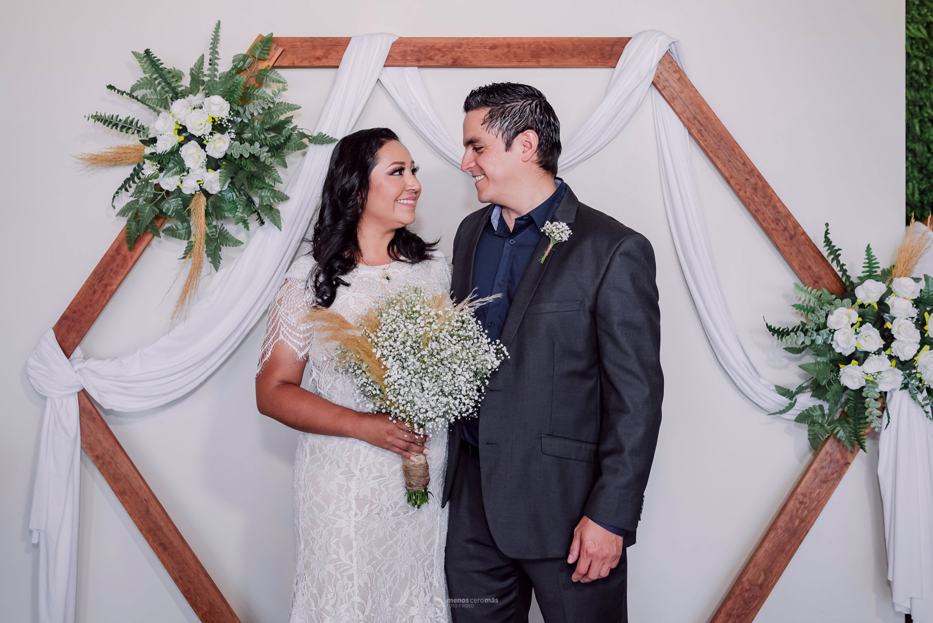 Fotografía de Raquel y José Luis en su boda civil celebrada en Corato Salón de Eventos, en Apodaca, México. La novia, vestida con un vestido blanco, sostiene su ramo en la mano. El novio, vestido con un traje negro, sonríe y mira a la novia.